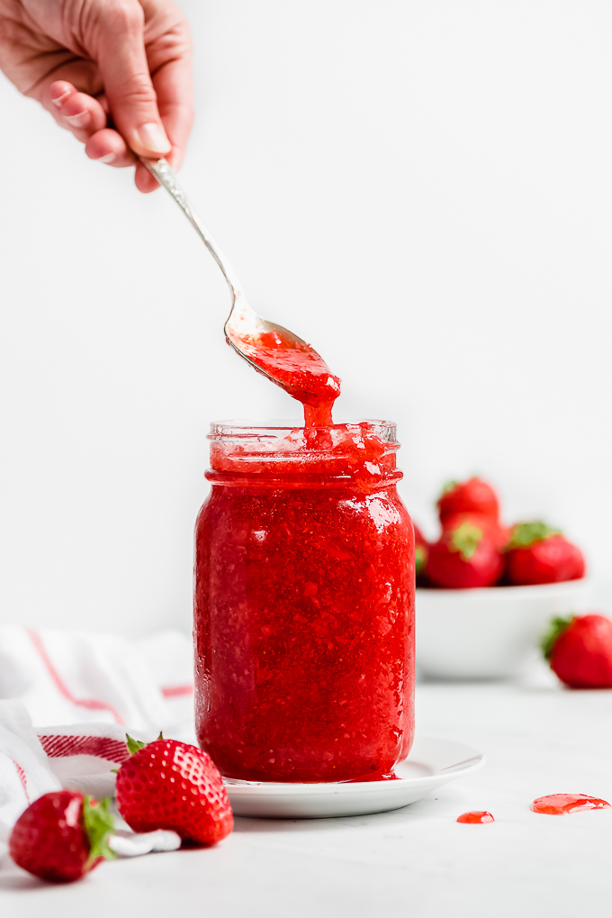 A hand lifting a spoonful of Strawberry Freezer Jam out of a mason jar.