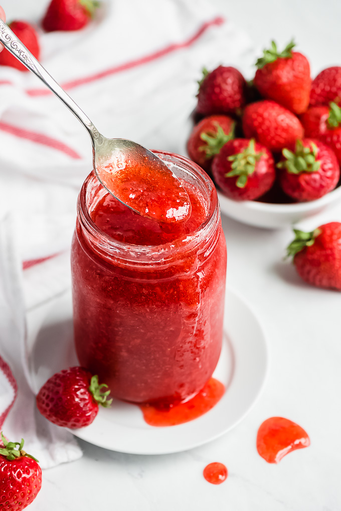 A close up of a spoonful and jar of Strawberry Freezer Jam.