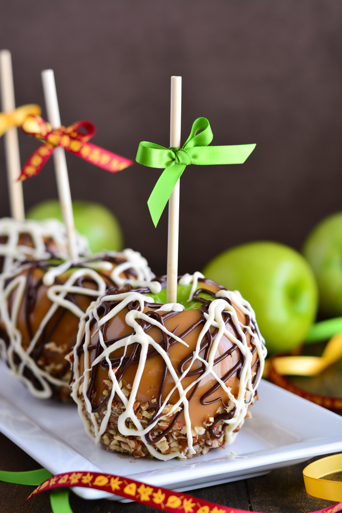 Close up shot of a caramel apple drizzled in chocolate and dipped in nuts.