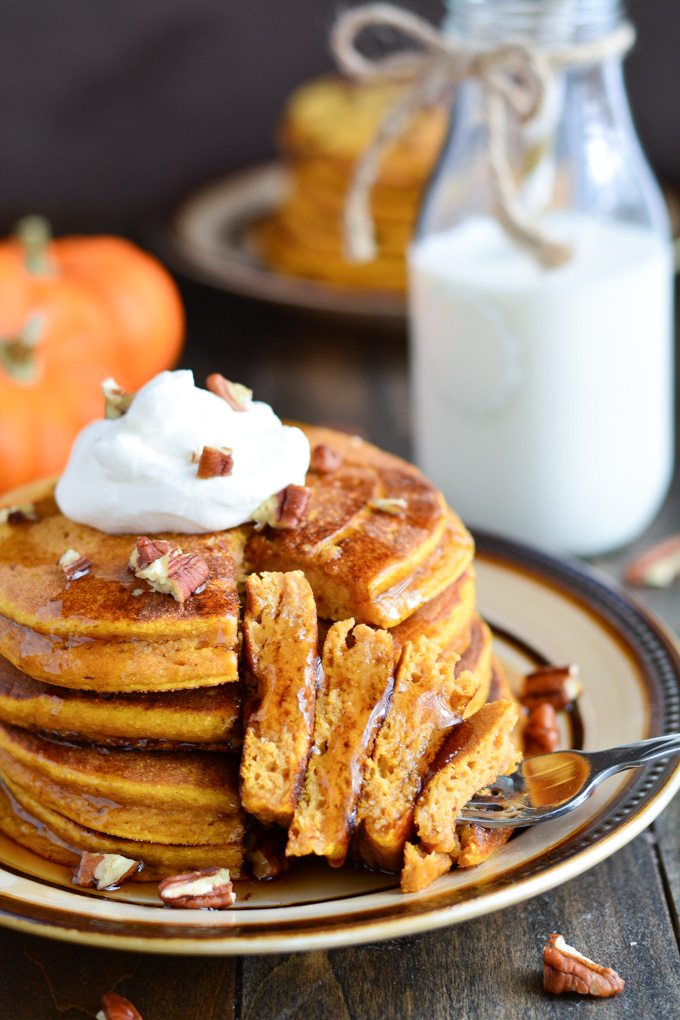 A stack of Whole Wheat Buttermilk Pumpkin Pancakes with a fork full from the stack with syrup drizzle on.