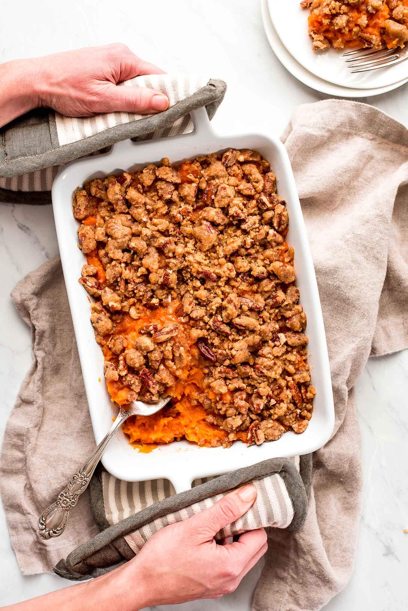 Someone holding a dish of Sweet Potato Casserole with hot pads.
