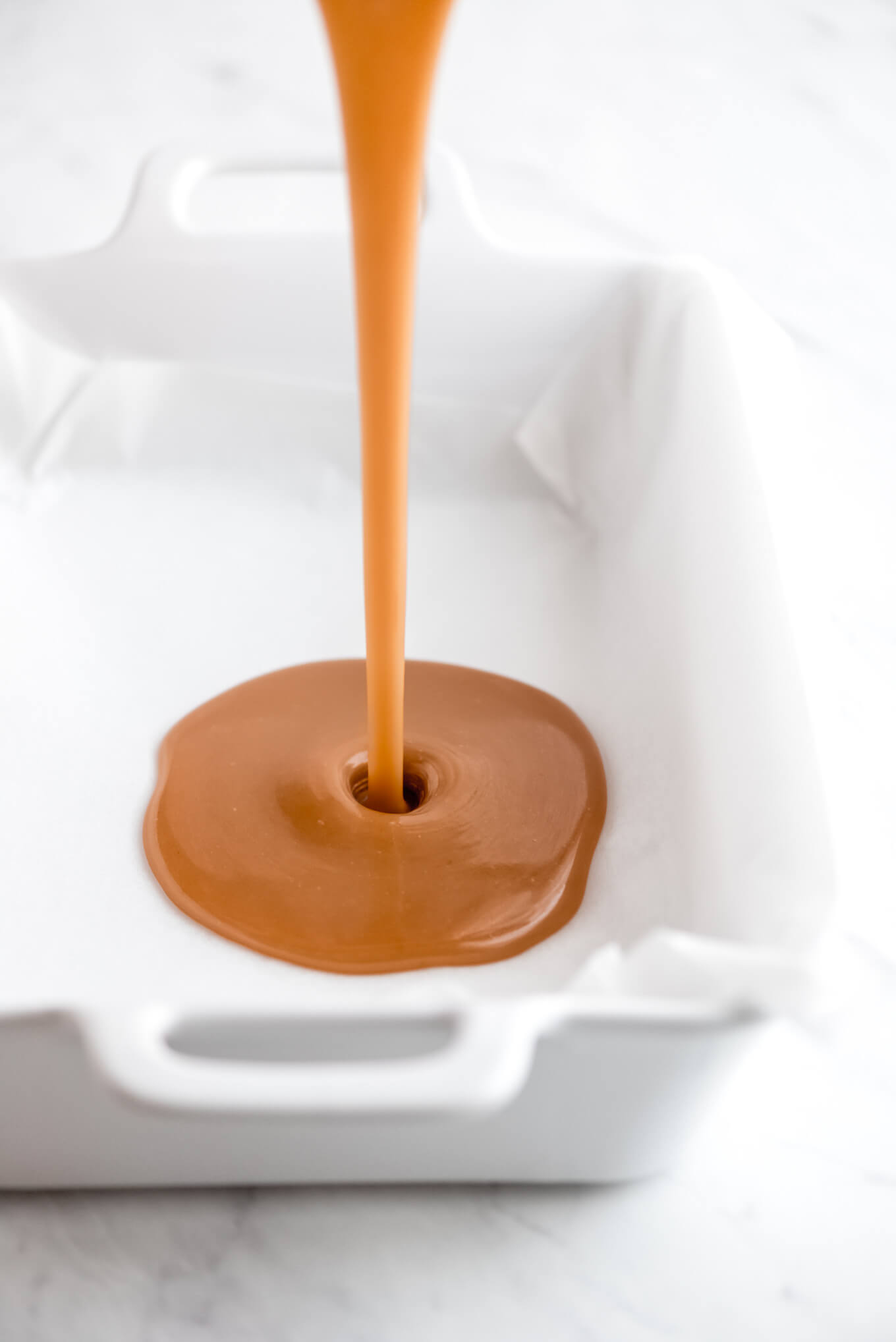 Hot caramel being poured into a parchment lined pan.