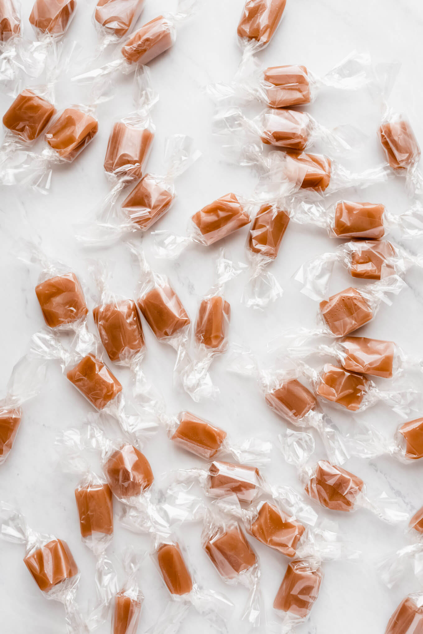 Many of Homemade Caramels wrapped in cellophane on a marble surface.