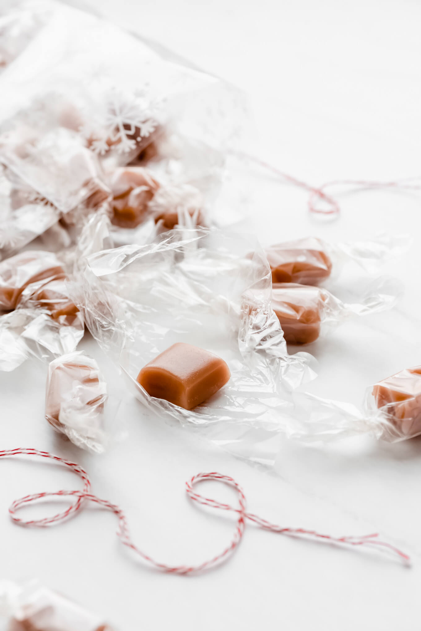 Caramels spilling out of a cellophane bag onto the table and one unwrapped.
