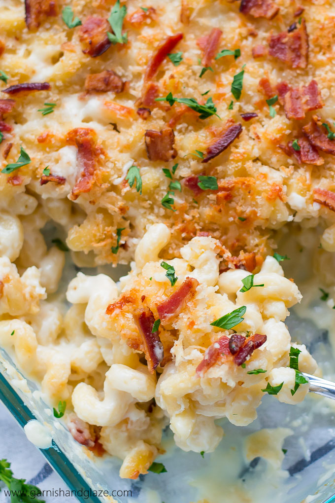Scooping a spoonful of creamy pasta topped with bacon, parsley, and bread crumbs out of a casserole dish.