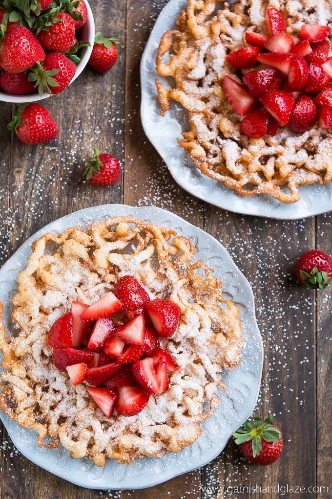 Bring the state fair to your home with these crisp and tender FUNNEL CAKES coated in powdered sugar and fresh strawberries!