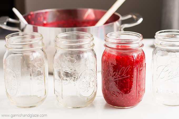Jars on a table with one full of fresh made Raspberry Freezer Jam.