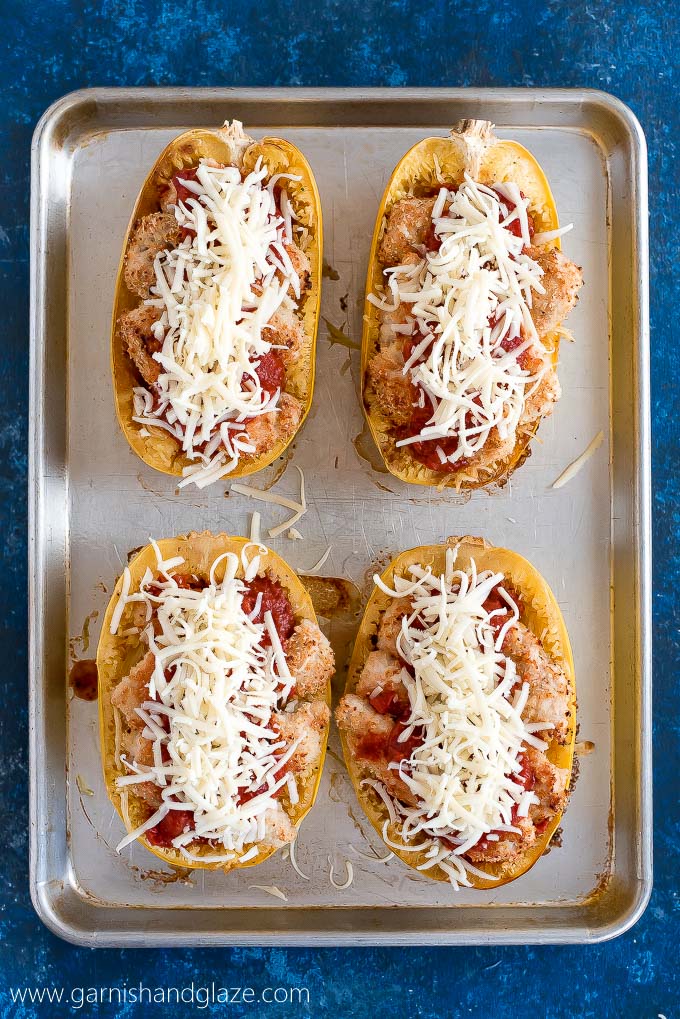 Four Chicken Parmesan Spaghetti Squash on a pan and topped with shredded cheese, ready to bake.