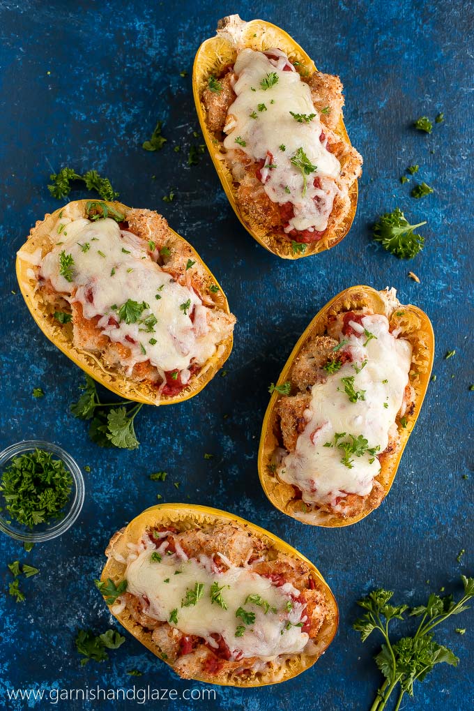 Four cooked spaghetti squash halves topped with Baked Chicken Parmesan, marinara sauce, cheese, and parsley.