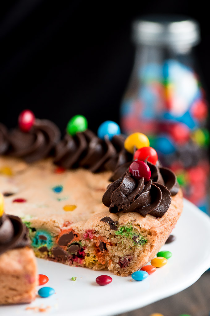 Close up of the inside of Chew M&M Cookie Cake topped with dark chocolate frosting.