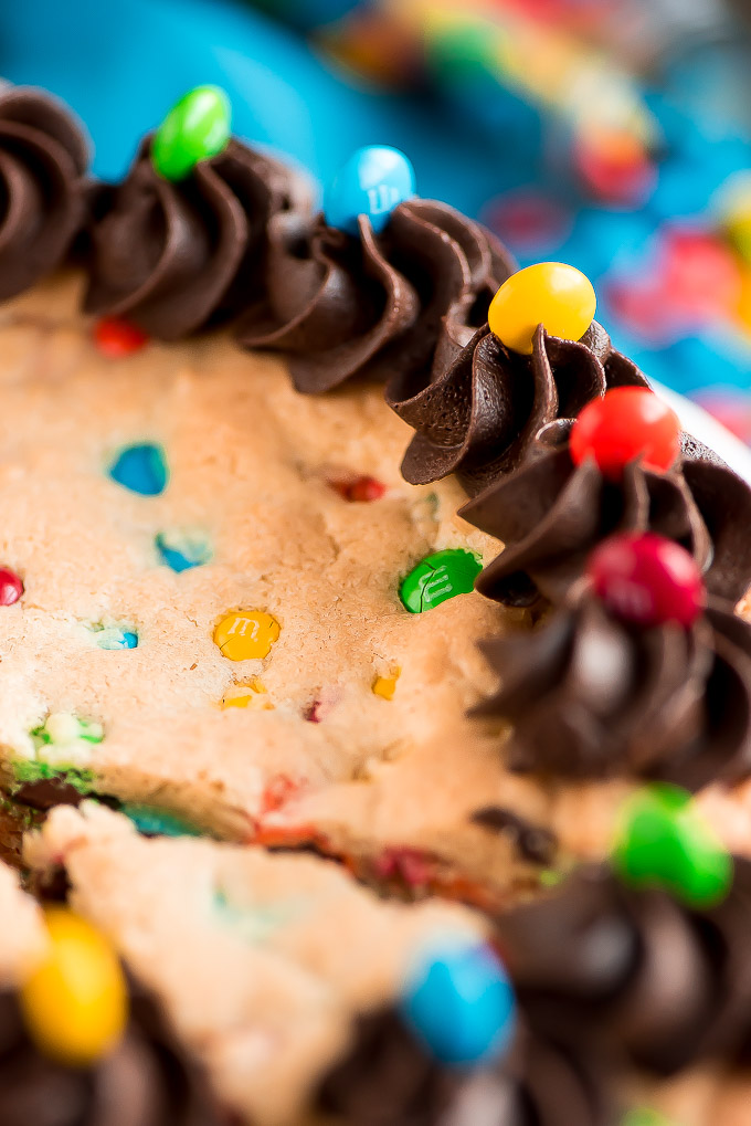 Close up of Chew M&M Cookie Cake topped with dark chocolate frosting piped on the edges.