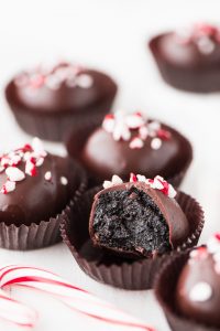 Chocolate dipped Peppermint Chocolate Oreo Truffles sprinkled with crushed candy cane sitting in a brown paper liner with a bite taken out showing the moist dark chocolate center.