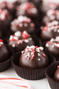 Chocolate dipped Pepper Mint Chocolate Oreo Truffles sprinkled with crushed candy cane sitting in brown paper liners.