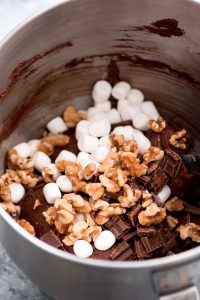 Chocolate cookie dough in mixing bowl with marshmallows, walnuts, and chocolate chunks thrown on top.