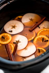 Slow Cooker Wassail in the slow cooker with lots of apple slices, orange slices, cinnamon sticks, and cloves floating in it.