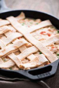 Chicken Pot Pie filling in a skillet with puff pastry dough strips on top forming a lattice.