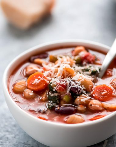 One bowl of Minestrone Soup packed with various vegetables, broth, beans, pasta, and sprinkled with Parmesan cheese.