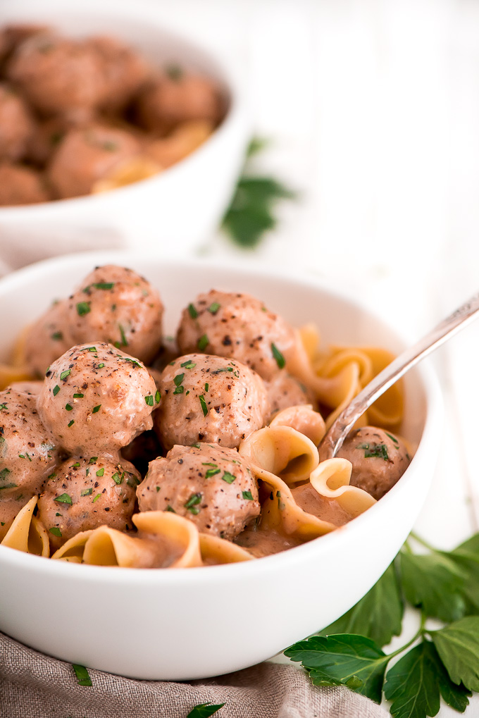 Bowl of Swedish Meatballs over egg noodles and garnished with pepper and parsley.