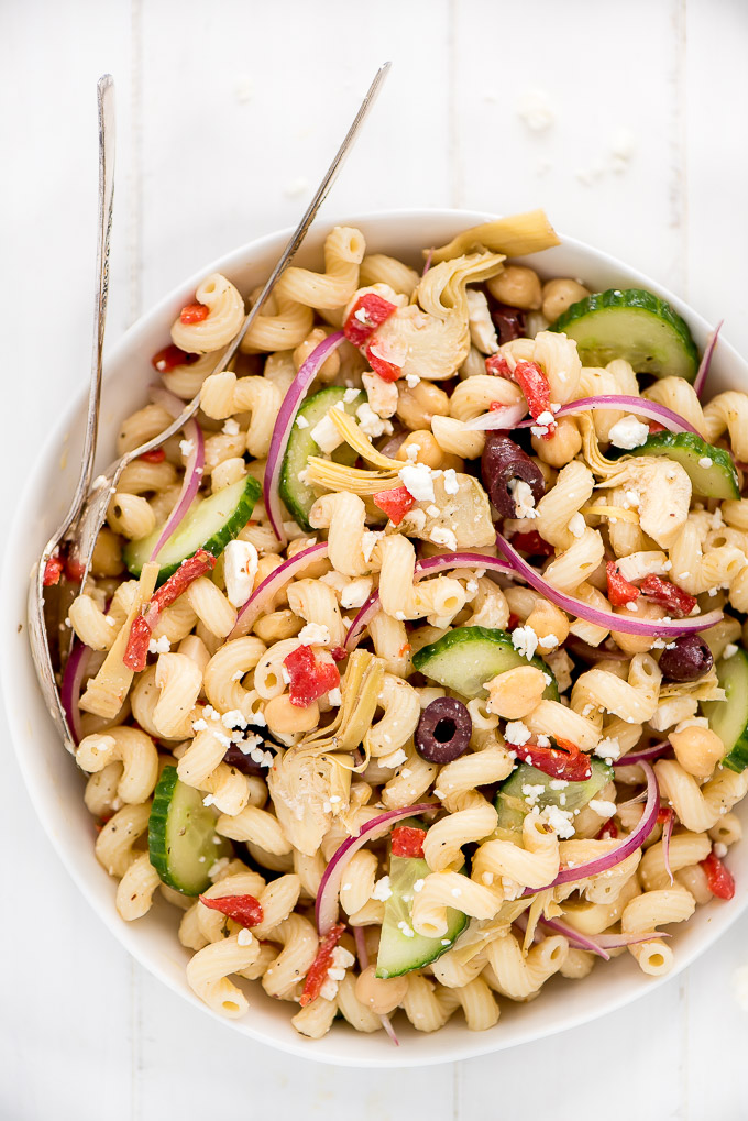 Serving bowl of Mediterranean Pasta Salad full of cavatappi noodles, kalamata olives, cucumbers, red onions, artichoke hearts, and pimientos.