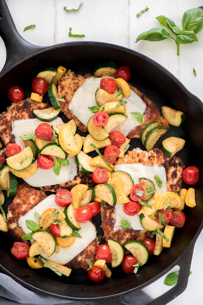 Chicken Parmesan in a skillet topped with fresh garden veggies.
