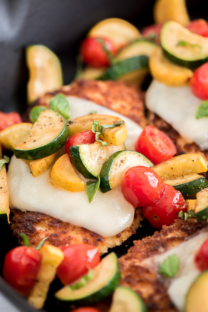 Close up of sauteed garden veggies on top of a mozzarella coated piece of chicken parmesan.