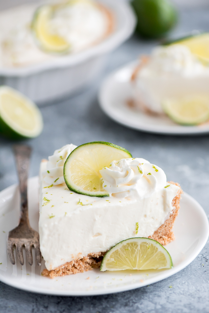 Close up of a slice of No Bake Key Lime Pie topped with whipped cream and a twisted lime slice.