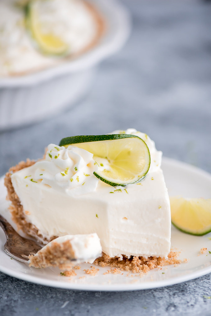 One slice of No Bake Key Lime Pie with a bit taken out of it topped with whipped cream and a lime slice.