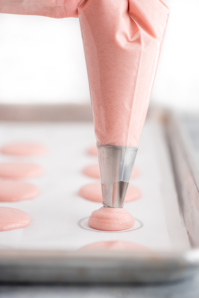 Piping pink macaron batter onto templet lined baking sheet.