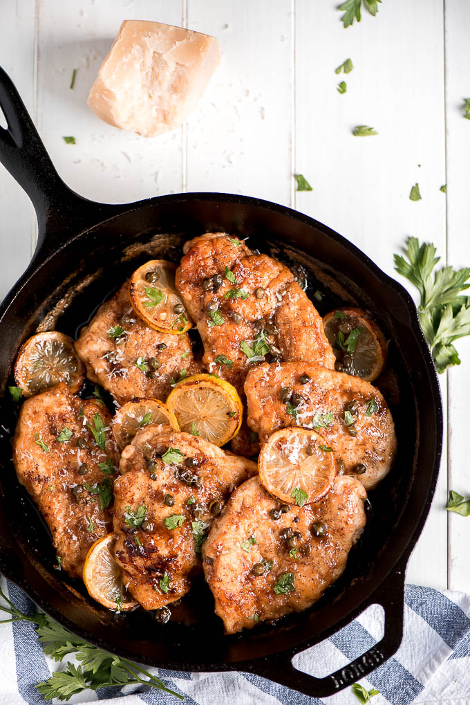 Lemon Chicken Piccata in a cast iron skillet topped with capers, parsley, and lemon slices.