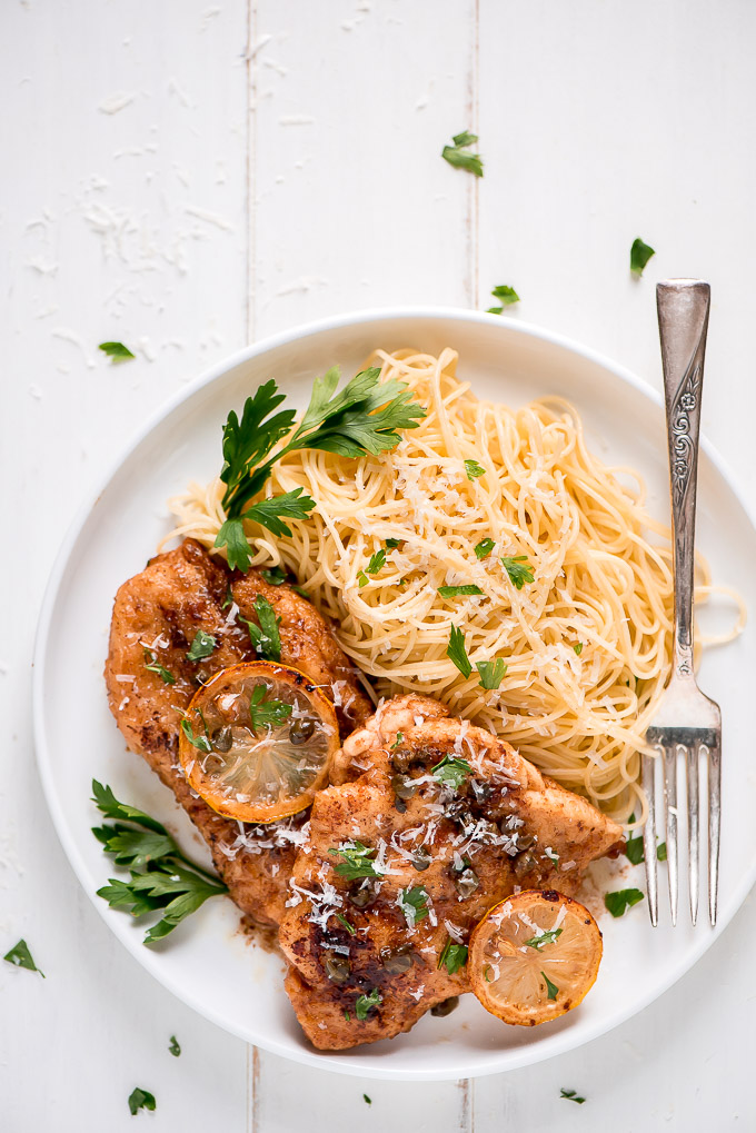 Lemon Chicken Piccata topped with capers, parsley, and Parmesan with a side of pasta.