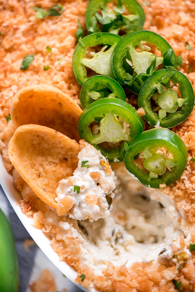 Close up top view of a couple chips in the casserole dish full of Spicy Jalapeno Popper Dip.