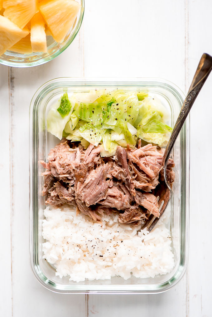 Meal Prep Kaula Pork in a glass containers along with rice, cooked cabbage and a side of pineapple.