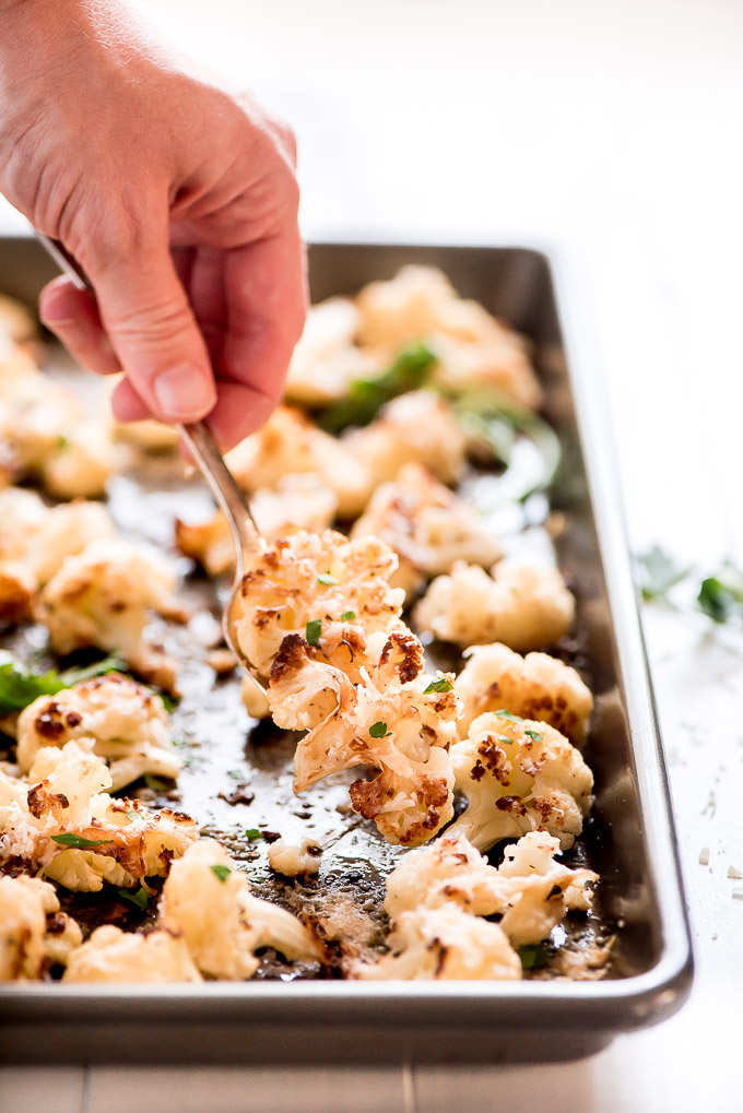 Scoping Parmesan Roasted Cauliflower garnished with parsley from off a sheet pan.