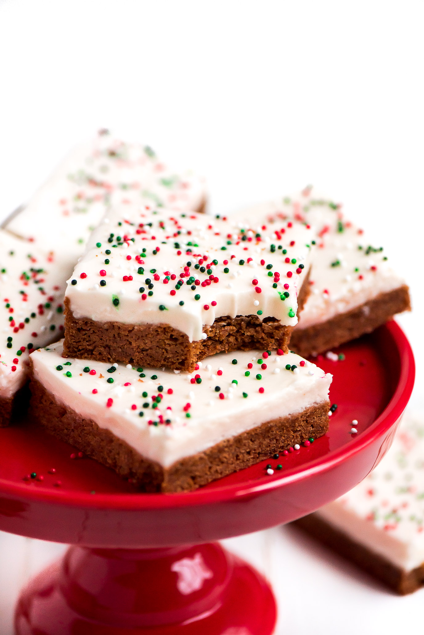 Gingerbread Sugar Cookie Bars on a red cake stand with a bite taken out of one.
