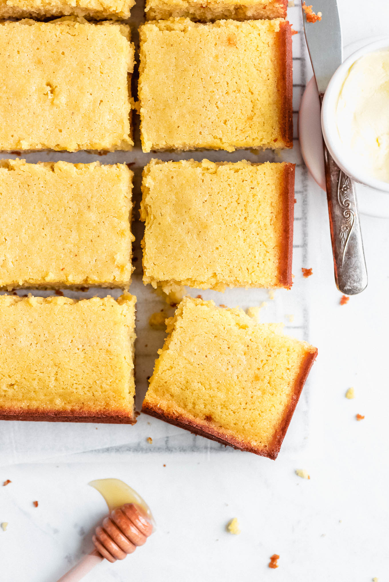 Cornbread square pieces on a cooling rack with a butter crock and honey stick on the side.