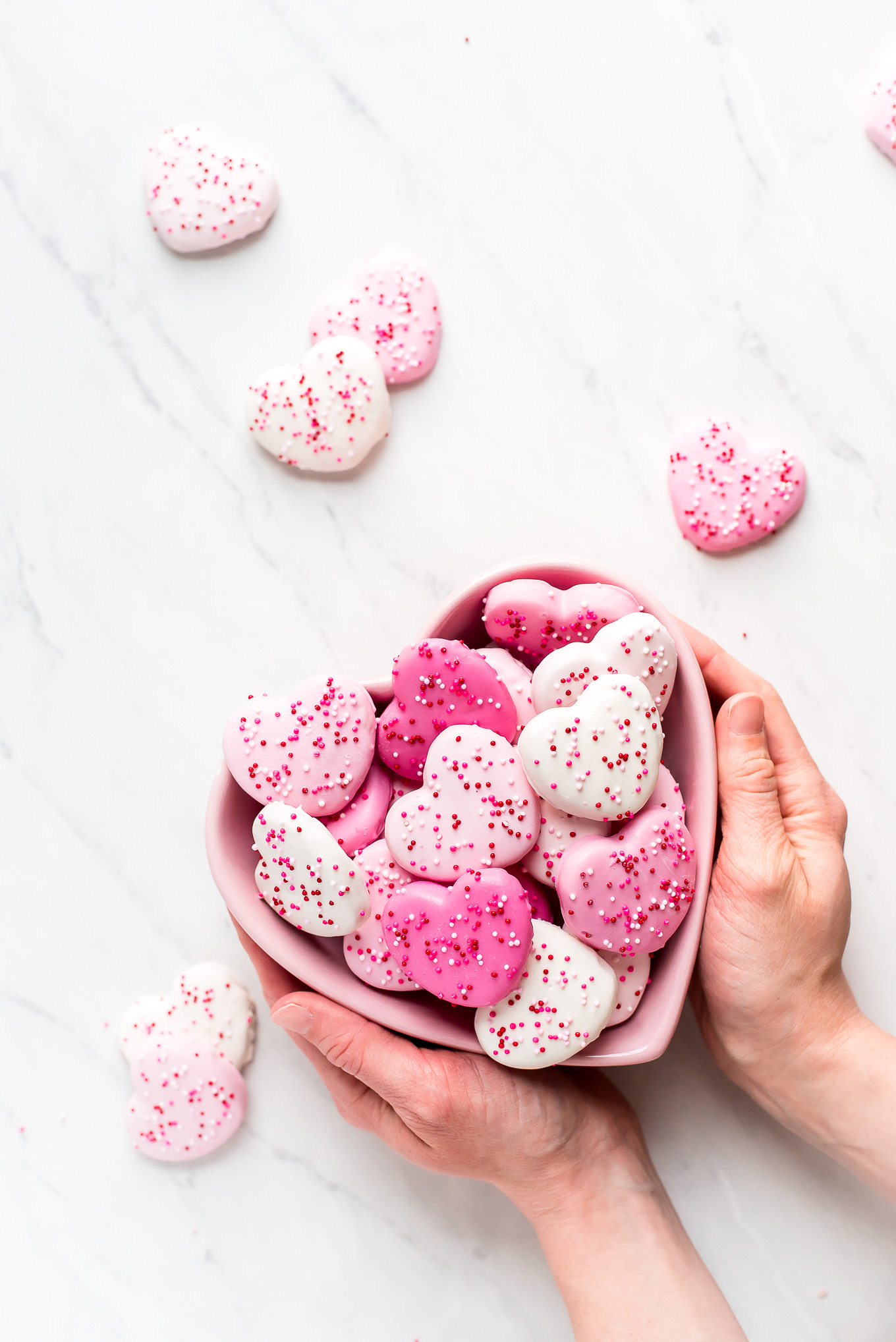 Pink & White Heart Circus Cookies in a heart shaped bowl with hands holding the bowl.