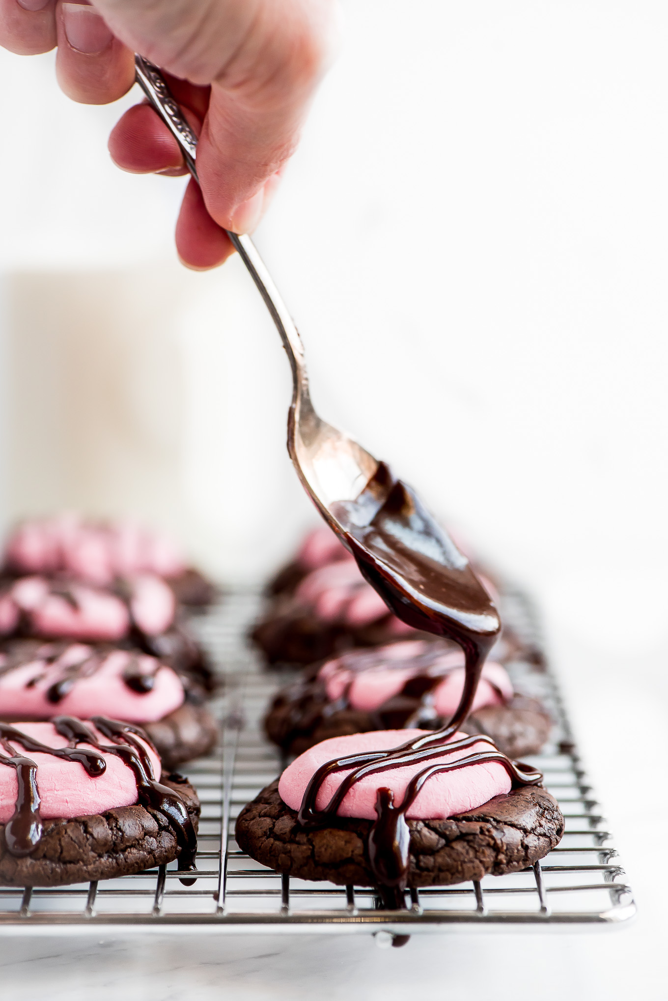Drizzling chocolate icing onto Chocolate Marshmallow Cookies that are sitting on a cooling rack.