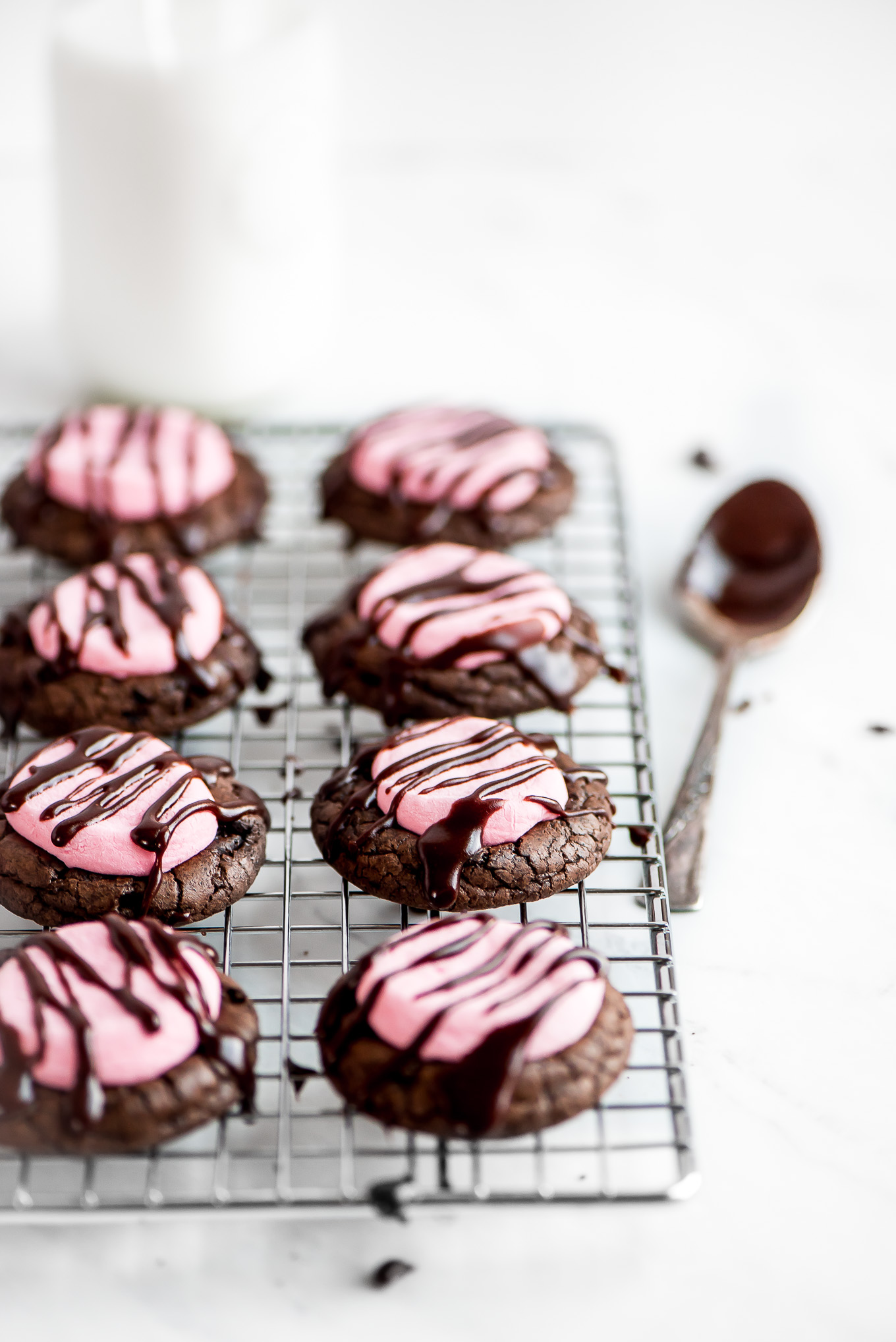 Strawberry Chocolate Marshmallow Cookies drizzled with chocolate icing, sitting on a cooling rack with a icing coated spoon to the side.