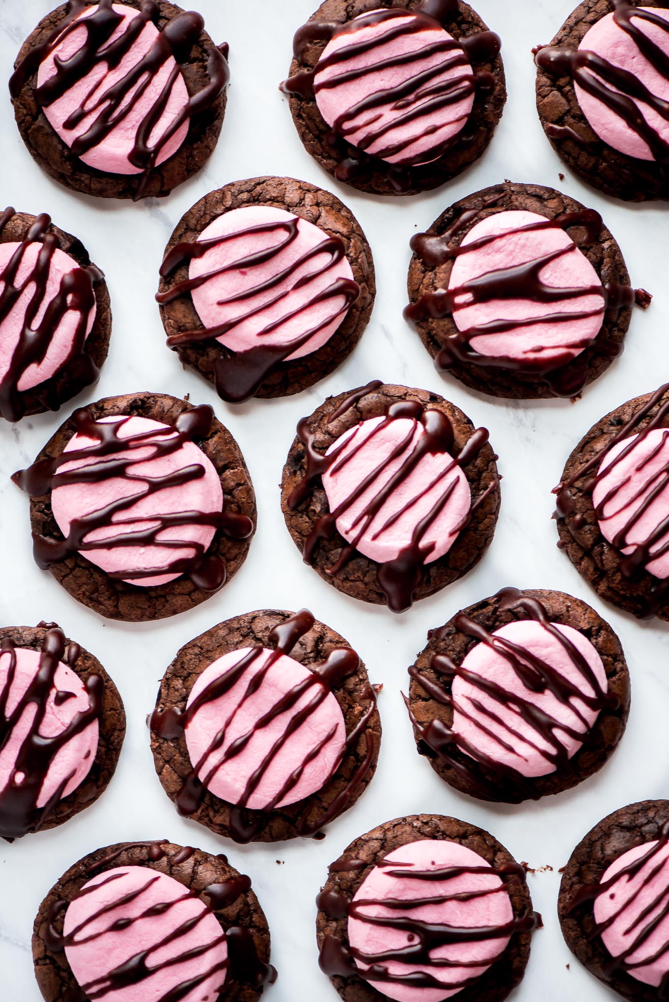 Many Marshmallow Cookies topped with a pink marshmallow and drizzled with chocolate icing.