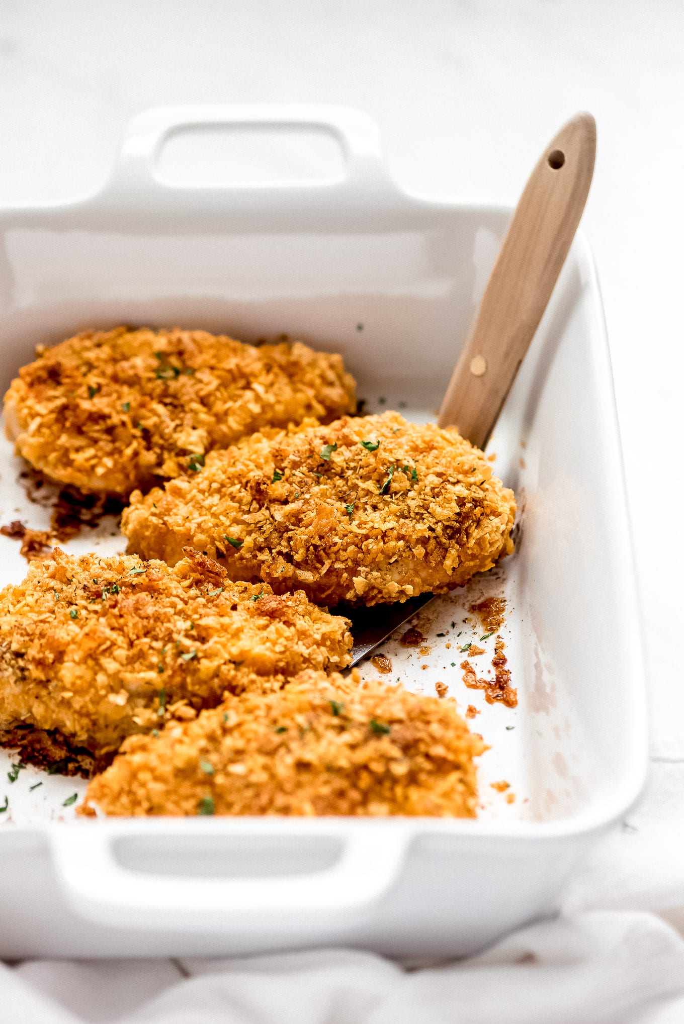 Healthy Cornflake Chicken sprinkled with parsley in a baking dish.