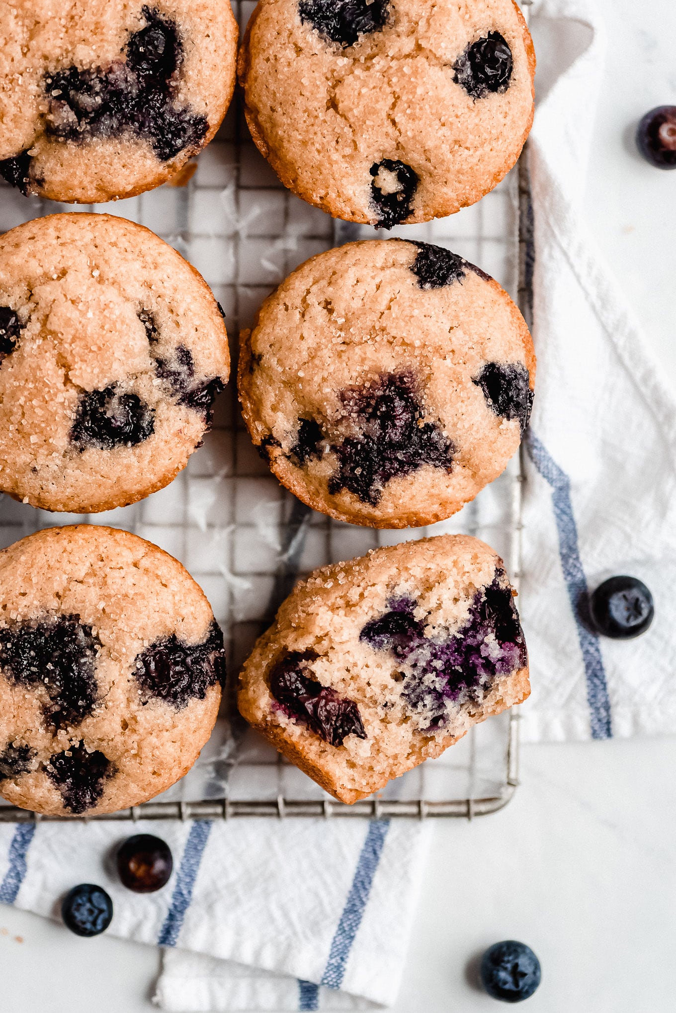 Greek Yogurt Blueberry Muffins on a cooling rack with one on it's side to show the fluffy tender texture and bursting blueberries.
