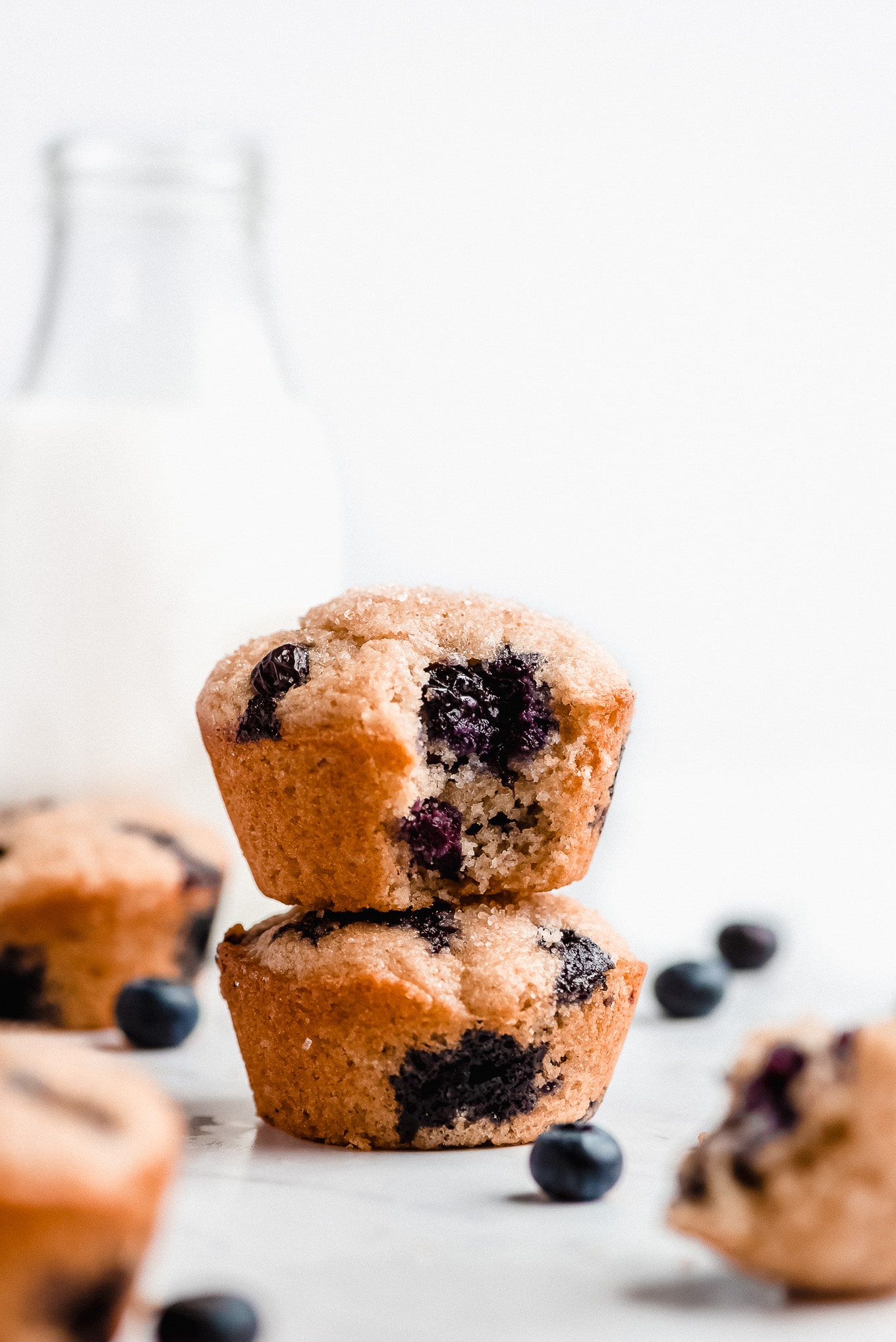 Greek Yogurt Blueberry Muffins stacked on top of each other. One has a bite taken out of it showing the moist tender crumb of the muffin.