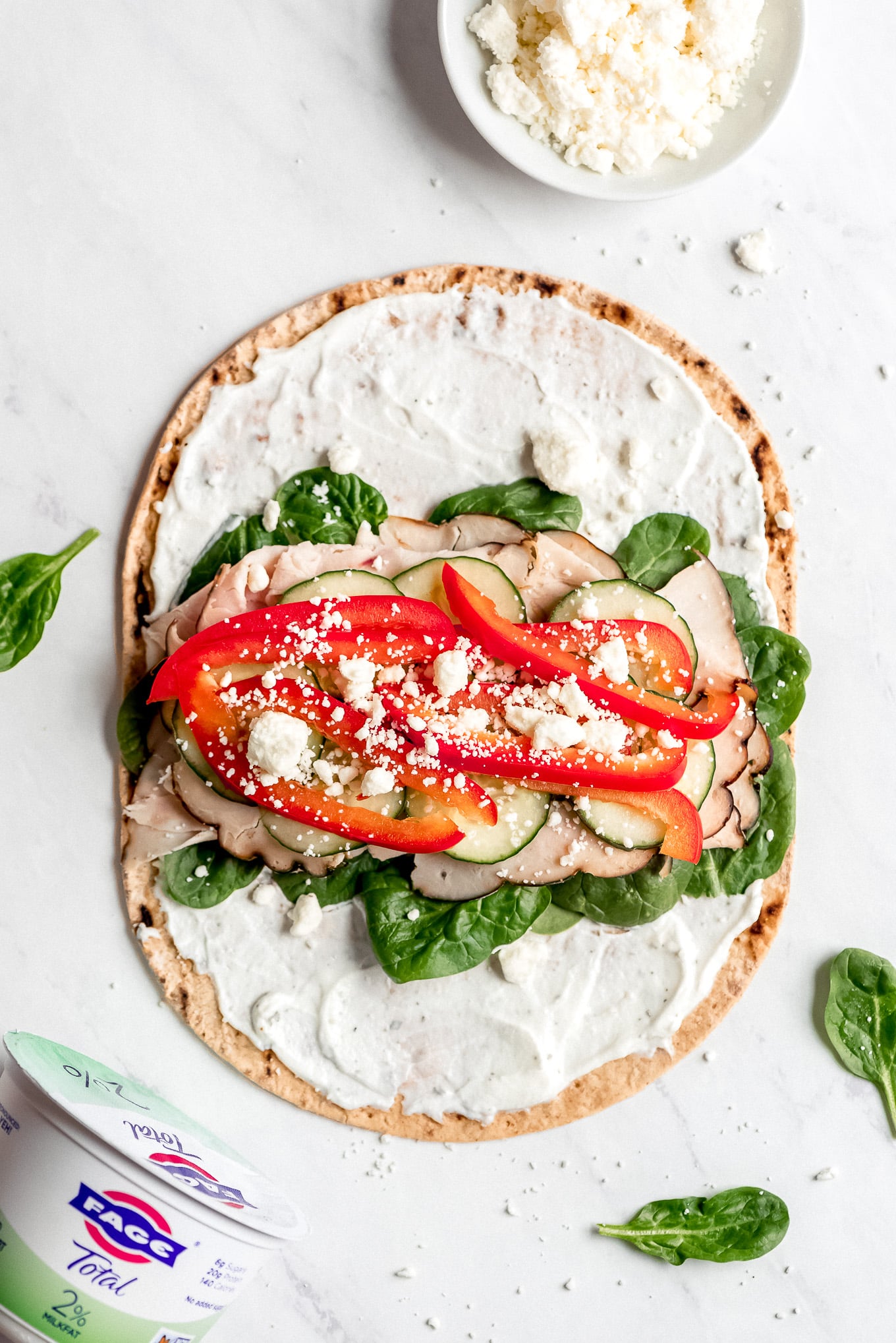 An open Turkey Ranch Wrap with Greek yogurt ranch sauce spread over the surface and then piled with spinach, turkey, cucumbers, bell peppers, and feta cheese.