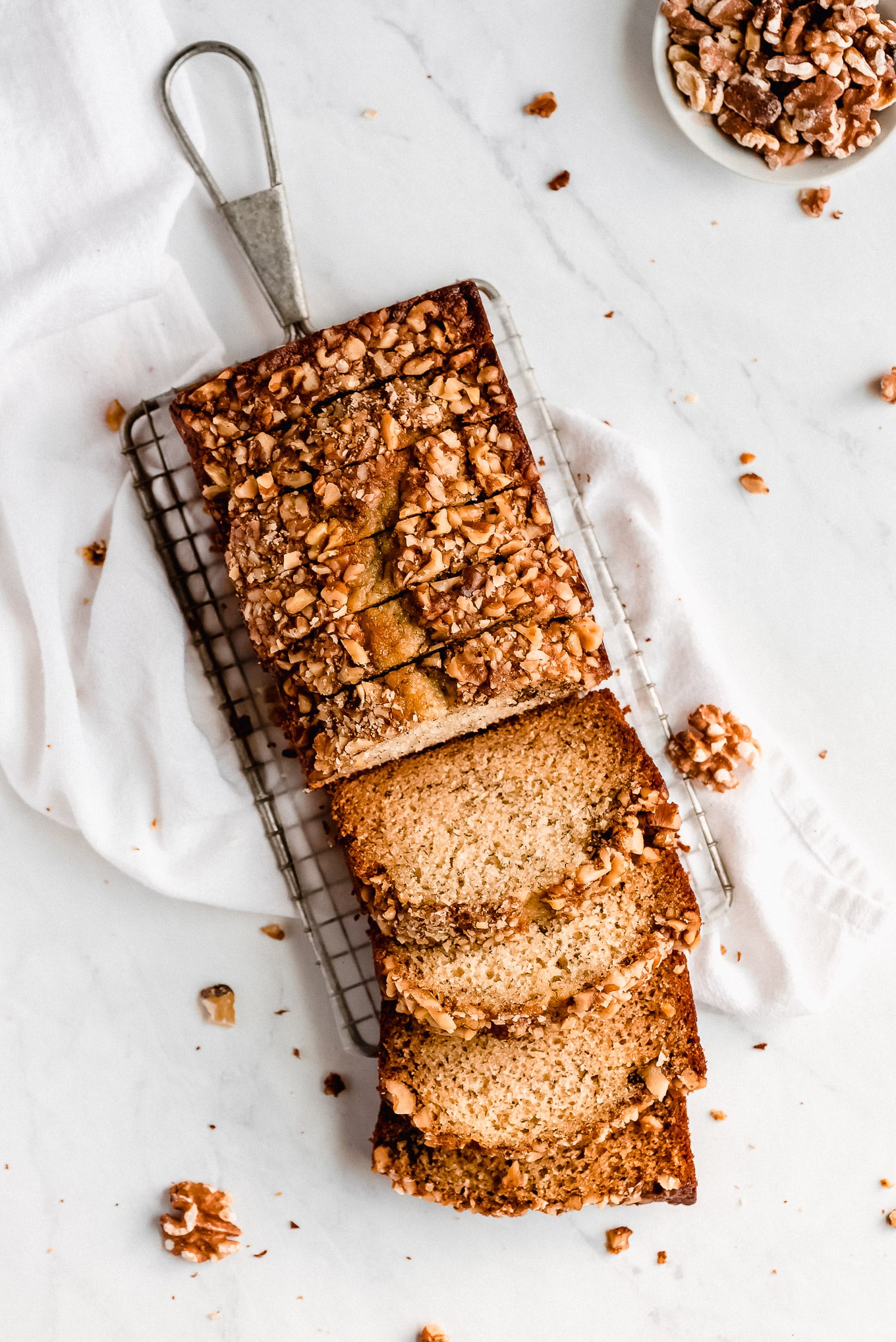 Banana Nut Bread sliced on a cooling rack with walnuts scattered around on the table.