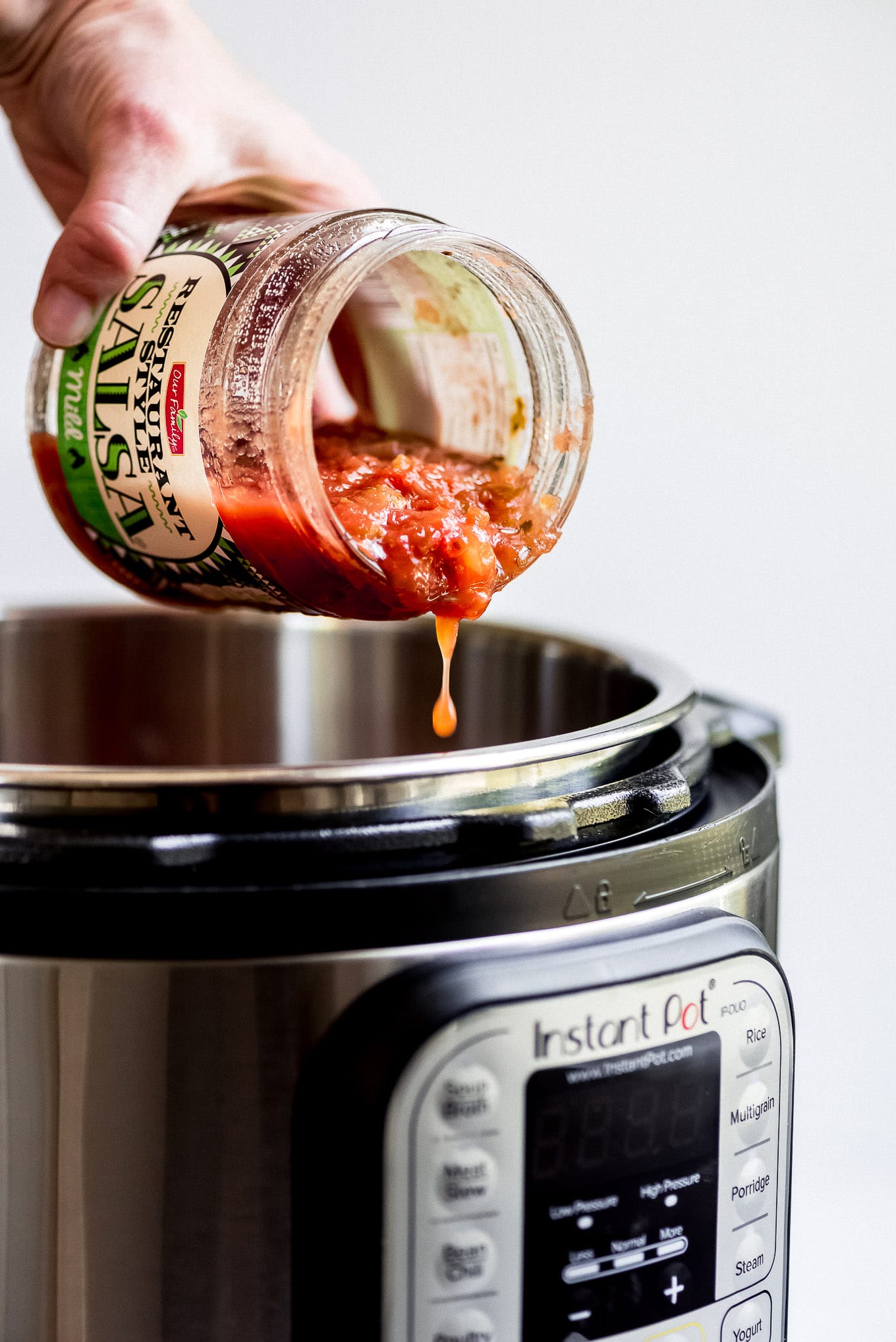 Pouring salsa out of a jar and into the Instant Pot for Salsa Chicken Tacos.