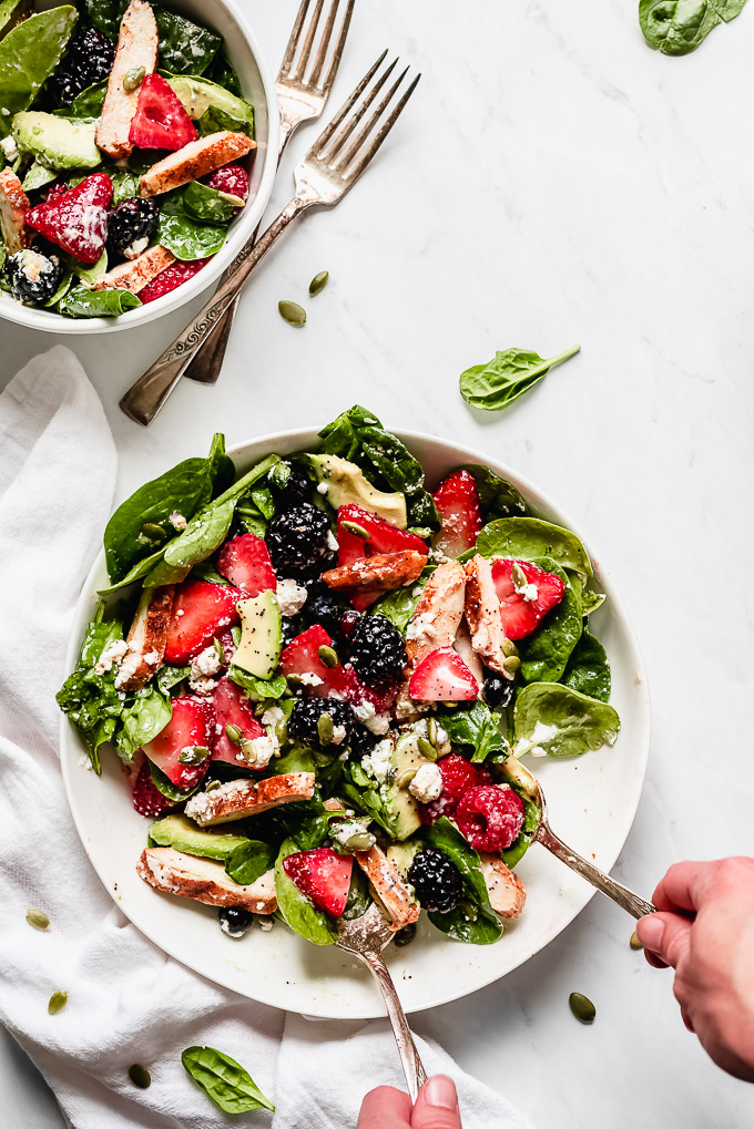 Berry Chicken Spinach Salad tossed together, being scooped out with two spoons and placed into a salad bowl.