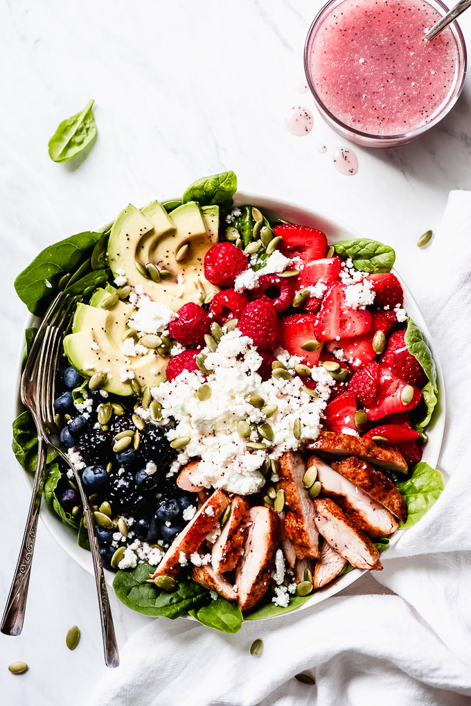 Berry Chicken Salad in a large bowl made up of grilled chicken, blackberries, blueberries, raspberries, strawberries, avocado slices, pepitas, goat cheese, and poppy seed dressing.