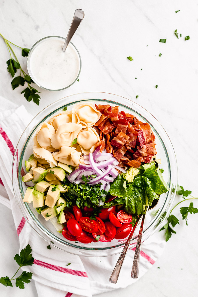Ingredients for BLT Pasta Salad in a large bowl with dressing in a small bowl to the side.