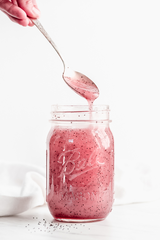 A large jar of pink poppy seed dressing with a spoon lifting some out and letting it stream back into the jar.