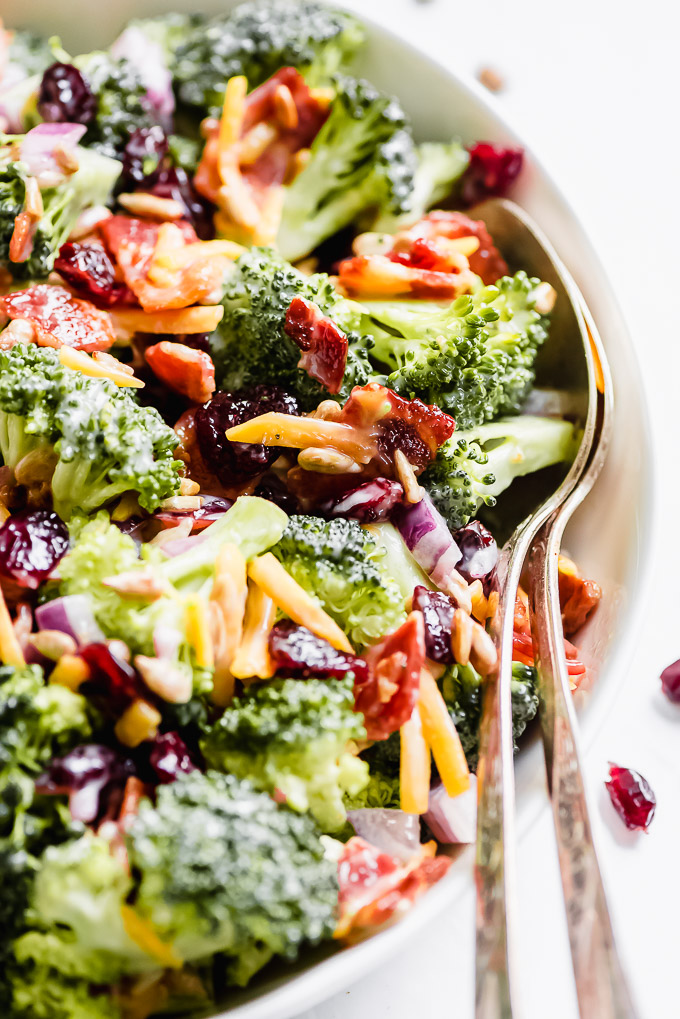 Close up of Broccoli Bacon Salad in a bowl showing the broccoli florets, bacon, cheese, dried cranberries, and onions.